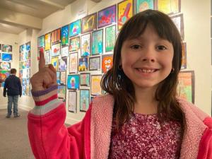 Cecilia-Cockerell-Austin-Elementary-1st-grade-pointing-to-her-artwork-titled-Parrot